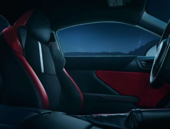 Interior view of a car with black and red seats and a dark night scene visible through the windows, creating a moody automotive image.