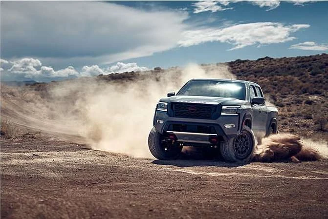 Nissan Frontier pickup truck drives across a desert landscape with dust billowing up from the tires, showcasing automotive performance.