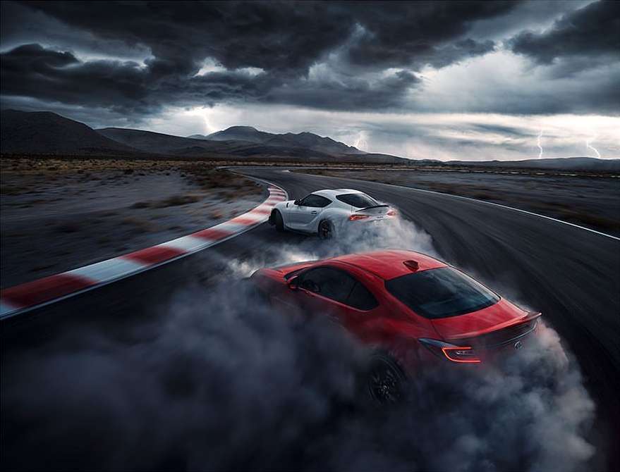 Two sports cars drifting on a racetrack with smoke billowing around them under a stormy sky with lightning, automotive photography.