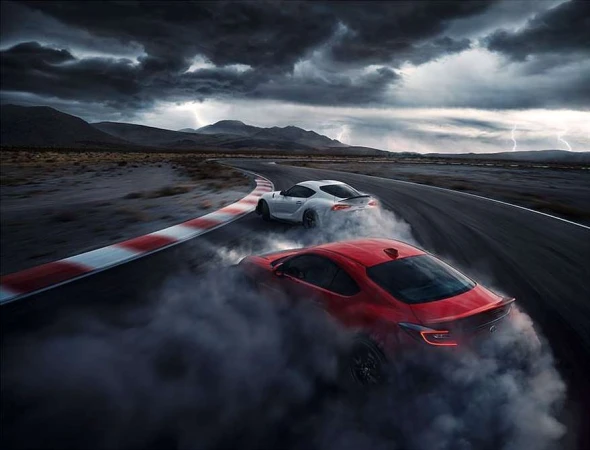 Two sports cars drifting on a racetrack with smoke billowing around them under a stormy sky with lightning, automotive photography.