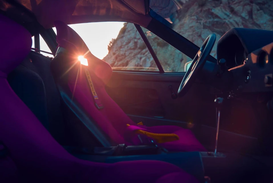 Interior view of a classic car featuring pink seats, a steering wheel, and a sunlit mountain visible through the windshield.