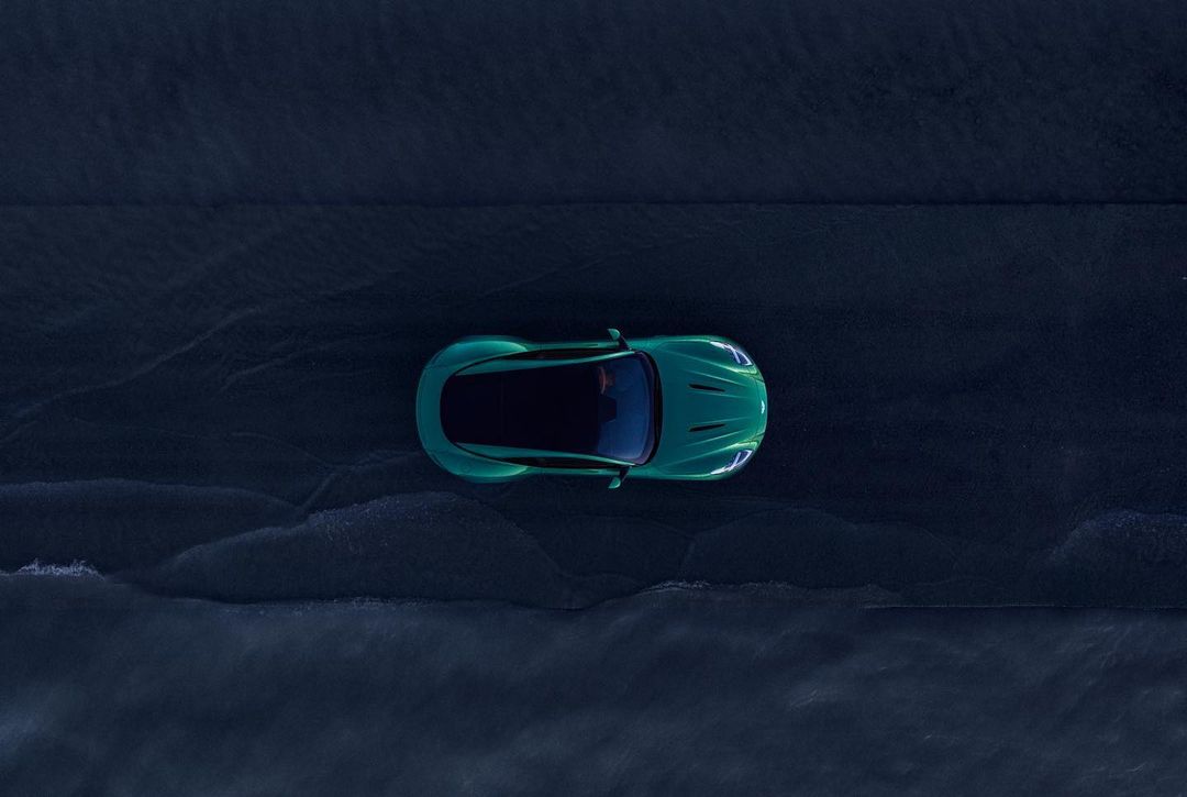 Overhead shot of a modern teal car on a wet asphalt surface with diffused lighting and a focus on automotive design and road presence.