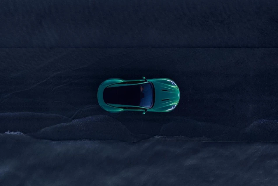Overhead shot of a modern teal car on a wet asphalt surface with diffused lighting and a focus on automotive design and road presence.