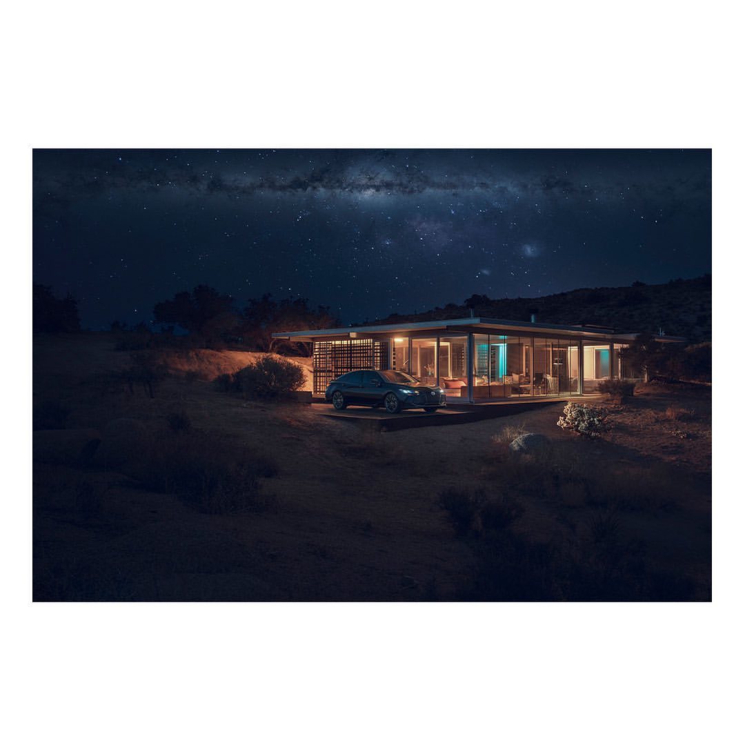 Exterior view of a modern house with a car parked outside, illuminated by lights and set against a starry night sky.
