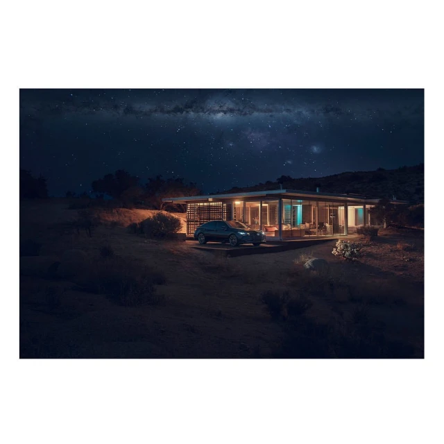Exterior view of a modern house with a car parked outside, illuminated by lights and set against a starry night sky.