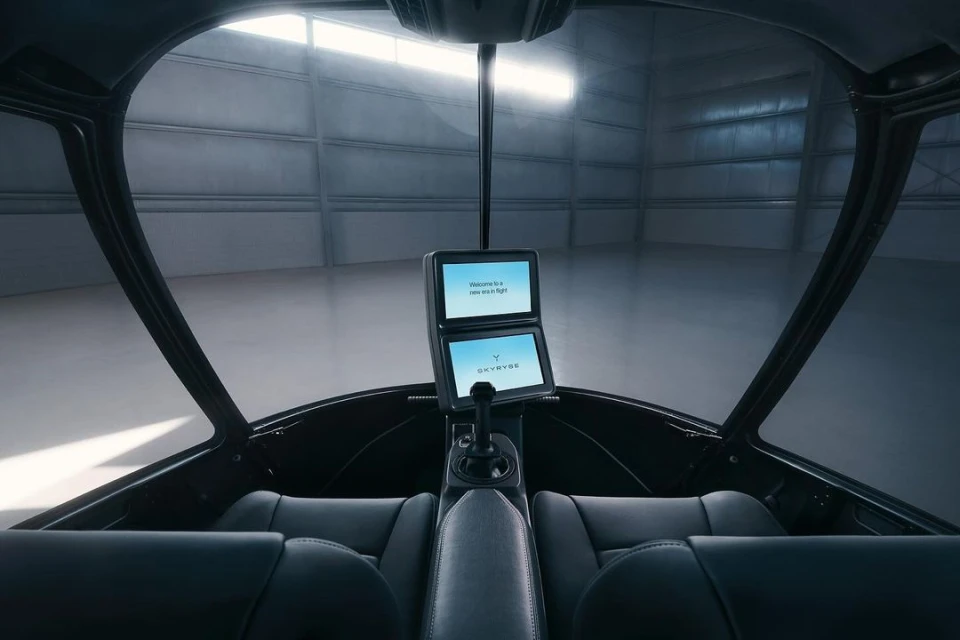 Interior view of Skyyvye aircraft cockpit featuring dual display screens, control stick, leather seats, and industrial hangar backdrop.