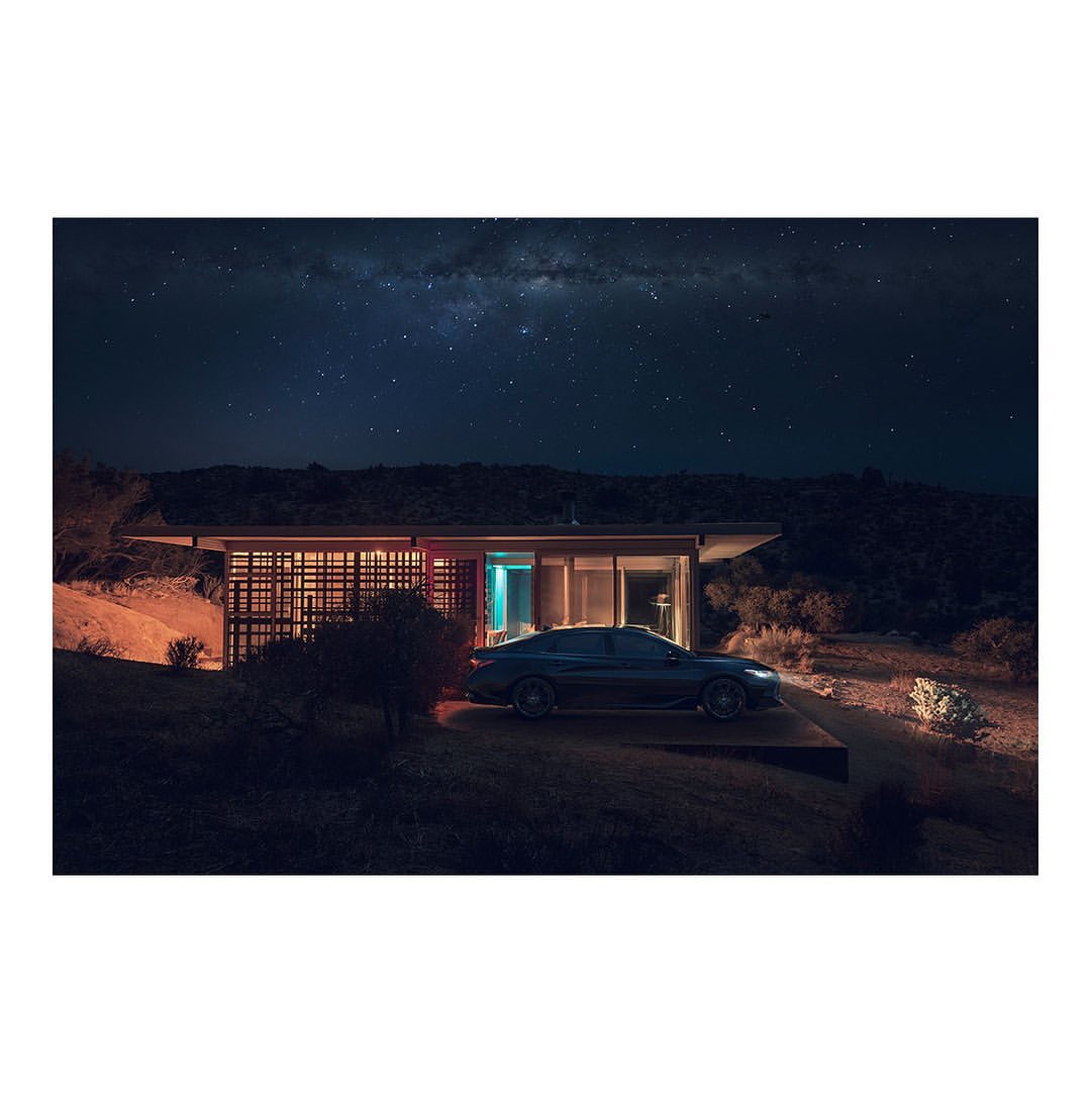 Modern house illuminated at night with a car parked outside, set against a backdrop of a dark sky filled with stars.