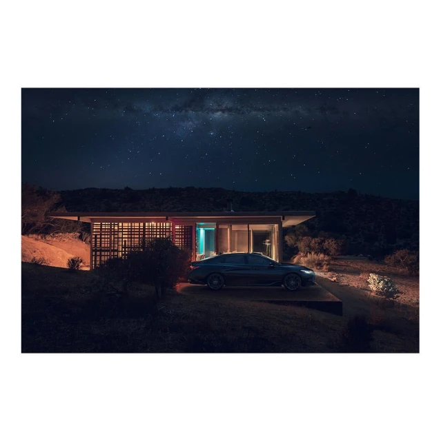 Modern house illuminated at night with a car parked outside, set against a backdrop of a dark sky filled with stars.