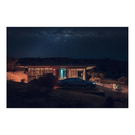 Modern house illuminated at night with a car parked outside, set against a backdrop of a dark sky filled with stars.