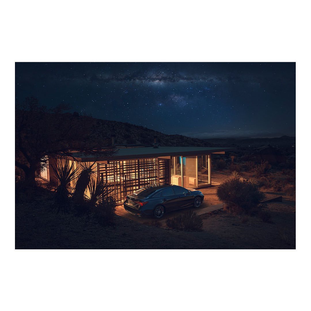 Contemporary house with a flat roof and expansive windows, illuminated at night with a car parked outside, set against a starlit sky.