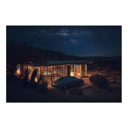 Contemporary house with a flat roof and expansive windows, illuminated at night with a car parked outside, set against a starlit sky.
