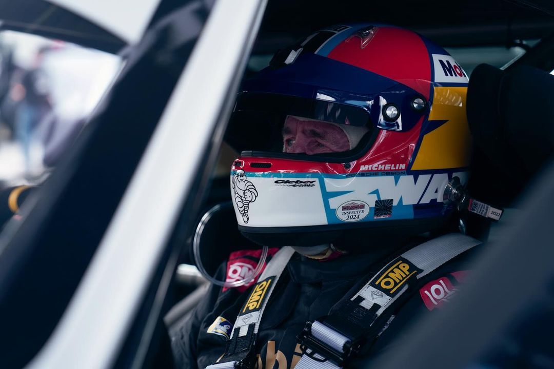 Close-up of race car driver with colorful helmet inside vehicle, wearing OMP branded safety equipment, providing a candid view.