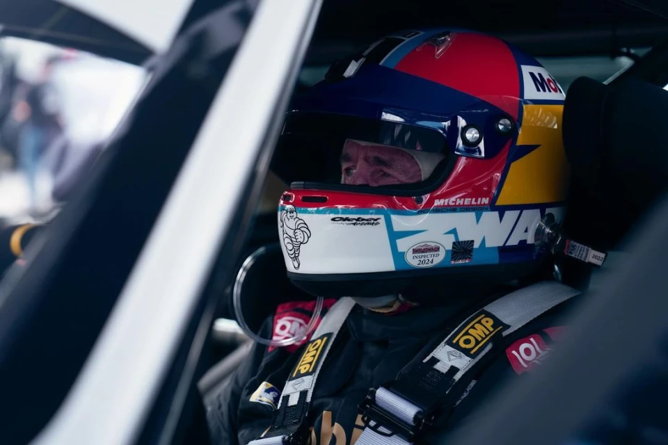 Close-up of race car driver with colorful helmet inside vehicle, wearing OMP branded safety equipment, providing a candid view.