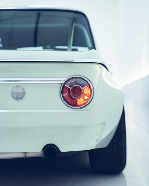 Rear view of a light-blue BMW 2002 featuring a round taillight, set against a neutral background, with a BMW logo emblem visible.