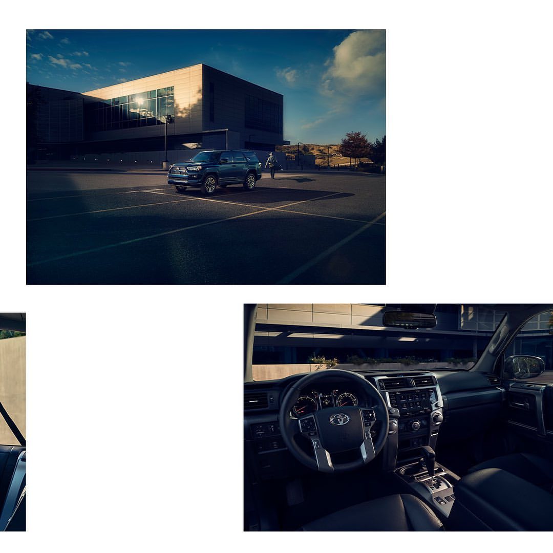 Blue SUV parked in an empty asphalt parking lot outside a modern glass and steel building under a clear blue sky