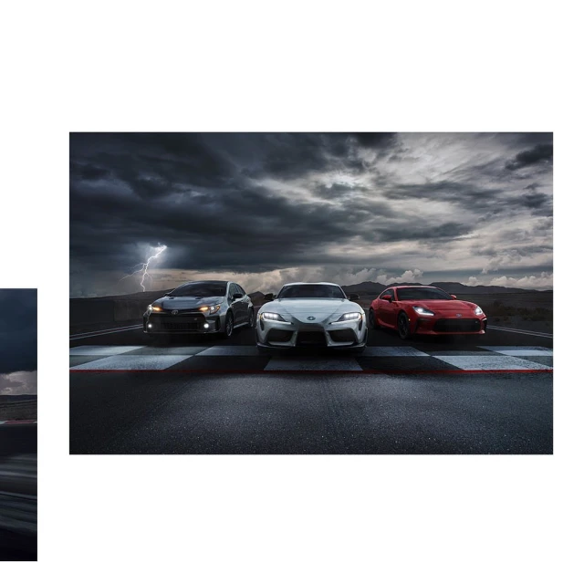 Three sports cars, a grey Subaru, a white Toyota Supra, and a red Toyota GR86, are parked on a racing track under a stormy sky with lightning.