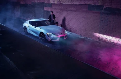 Man standing next to a white sports car parked in a neon-lit alleyway with smoke swirling around.