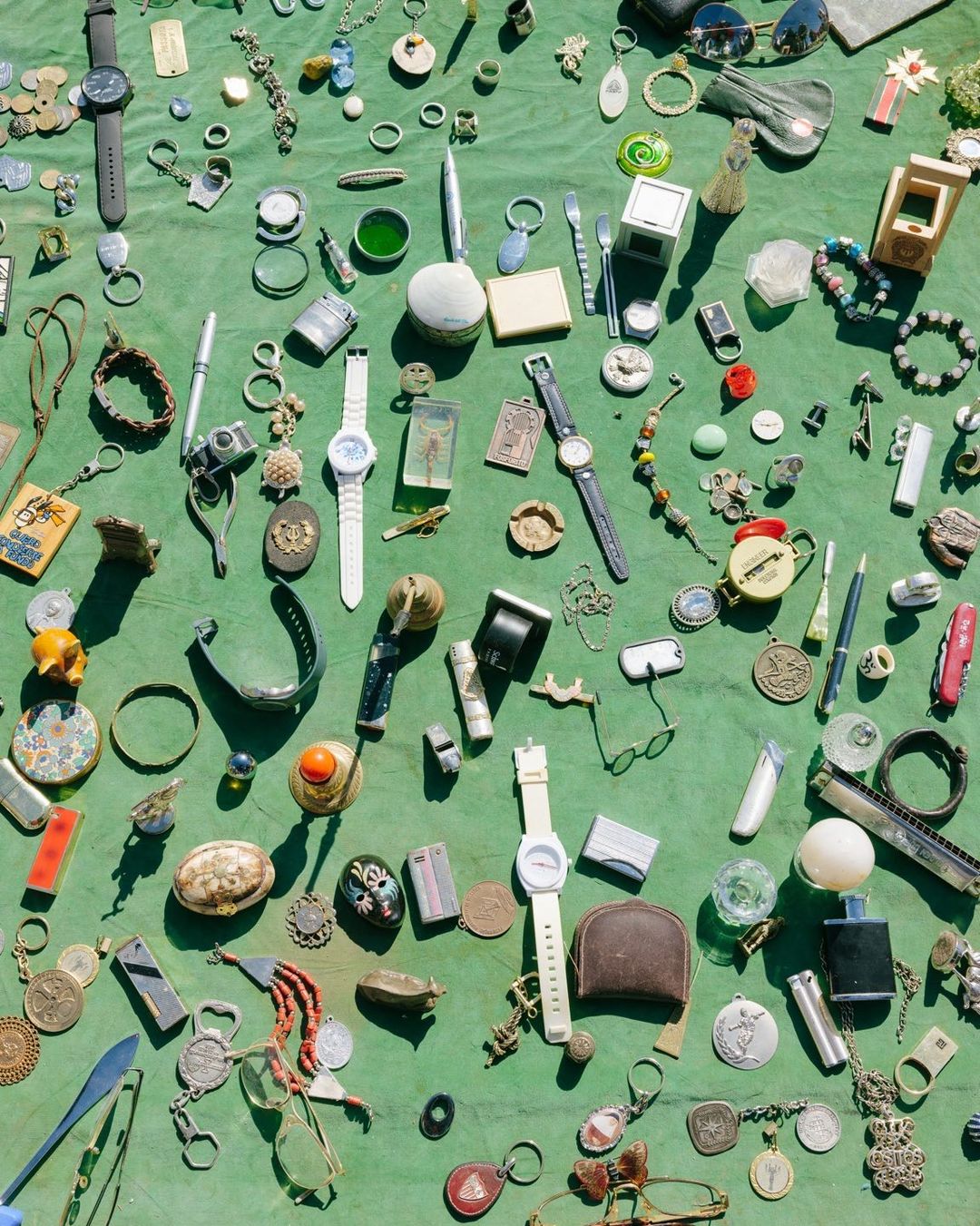 Overhead shot of many vintage and antique objects on a green surface, including watches, glasses, jewelry, and various trinkets.