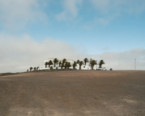 White villa surrounded by palm trees set on a flat, barren terrain under a partly cloudy sky captured by Alex Cretey Systermans.