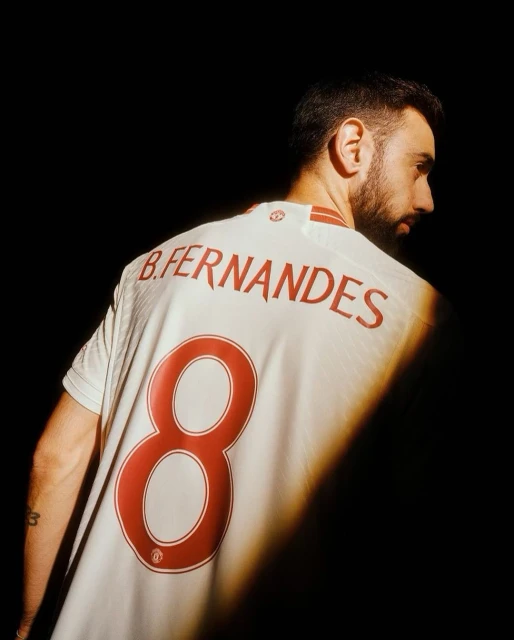 Close-up of male soccer player wearing a white jersey with the number 8 on the back against a dark background. Athletic apparel. 