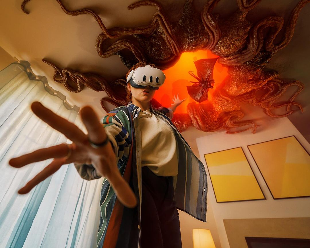 Woman wearing a VR headset reaches toward the camera; a digitally-rendered portal with tentacles is visible on the ceiling above.
