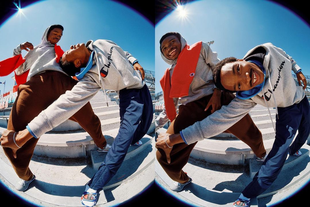 Two young African-American men in Champion hoodies pose on concrete stadium steps under a bright sun, captured with a fisheye lens.