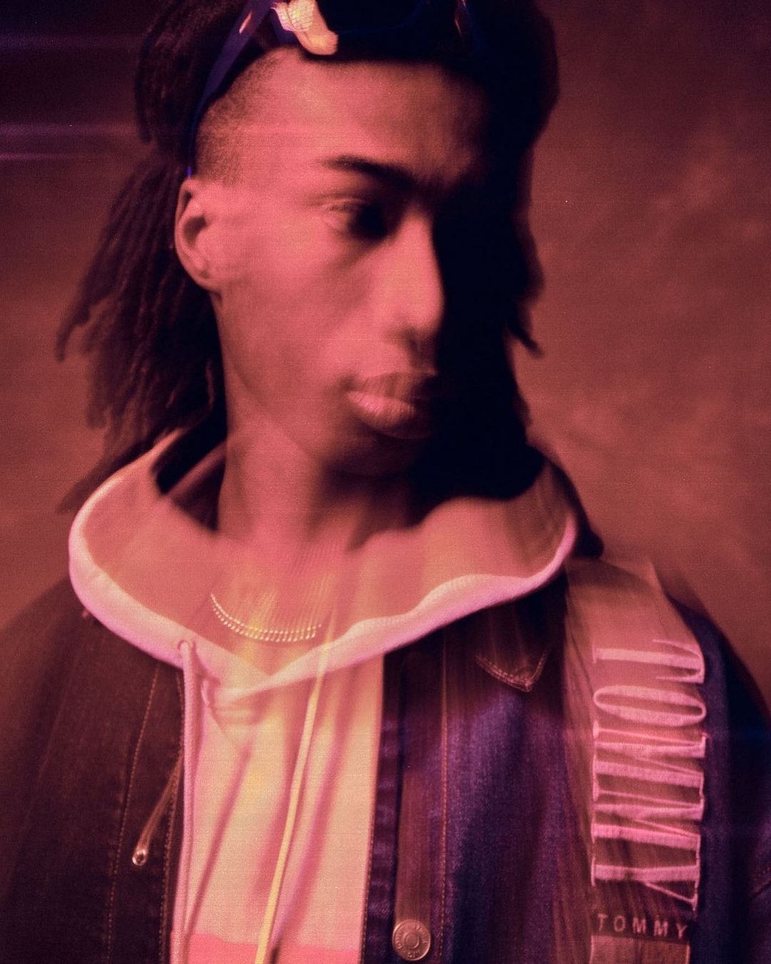 Portrait of a young adult male wearing a headscarf, denim jacket, and hooded sweatshirt; shot with a strong magenta color grade.