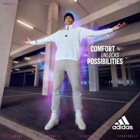 An adult man in athletic apparel stands with arms spread in an urban parking garage setting, showcasing modern athletic wear.