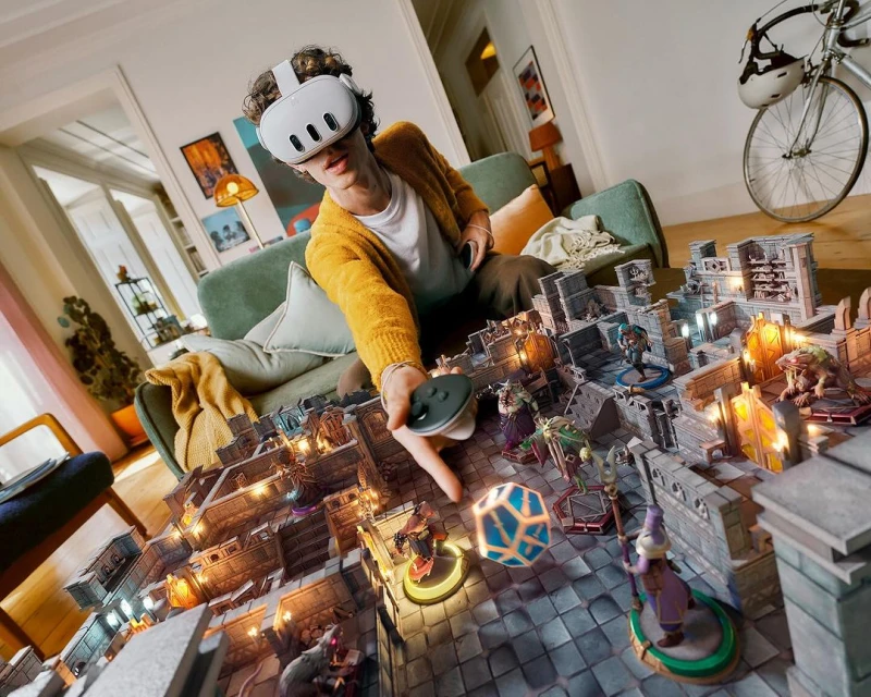 A person wearing a VR headset sits on a couch, appearing to manipulate a fantasy tabletop game with miniatures, dice, and fantasy architecture.
