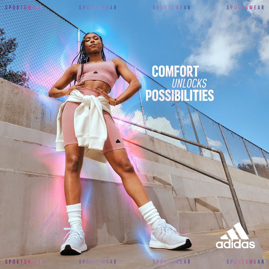 Athletic woman in sportswear standing on a concrete surface with a fence and sky visible in the background for an Adidas sportswear ad.