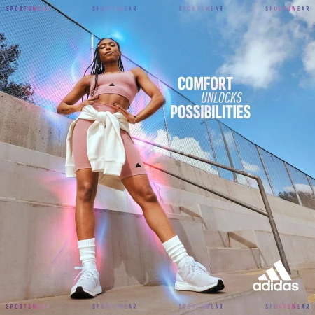 Athletic woman in sportswear standing on a concrete surface with a fence and sky visible in the background for an Adidas sportswear ad.