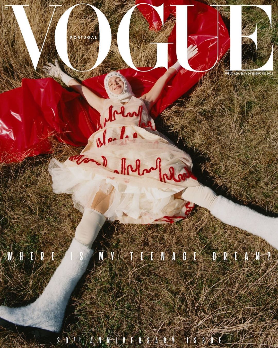 Vogue Portugal cover featuring a model in a white dress and long white socks lying on a field with a red sheet behind her.