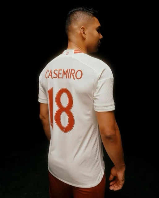 Soccer player Casemiro in a white jersey with red number 18, set against a dark background. Profile view focusing on uniform details.
