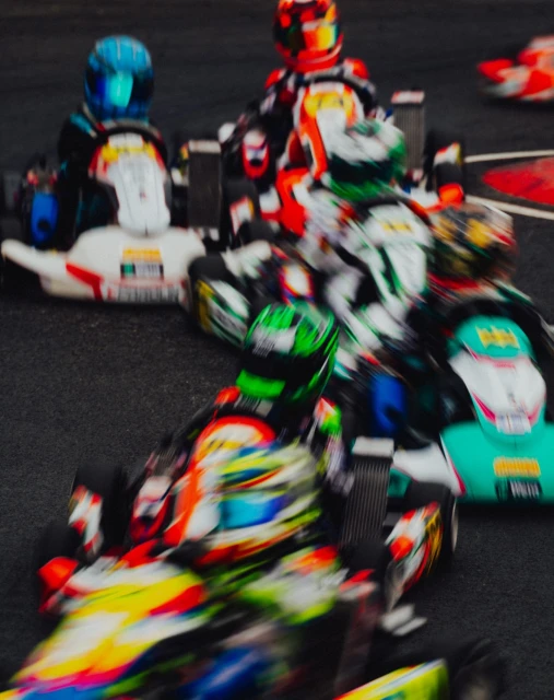High-speed go-kart race with multiple racers in colorful helmets and racing suits competing on an asphalt track, captured with motion blur.