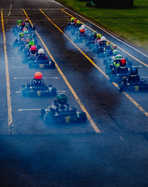 Go-kart racing on a track with a line of racers speeding towards the finish line in a high-speed competition.