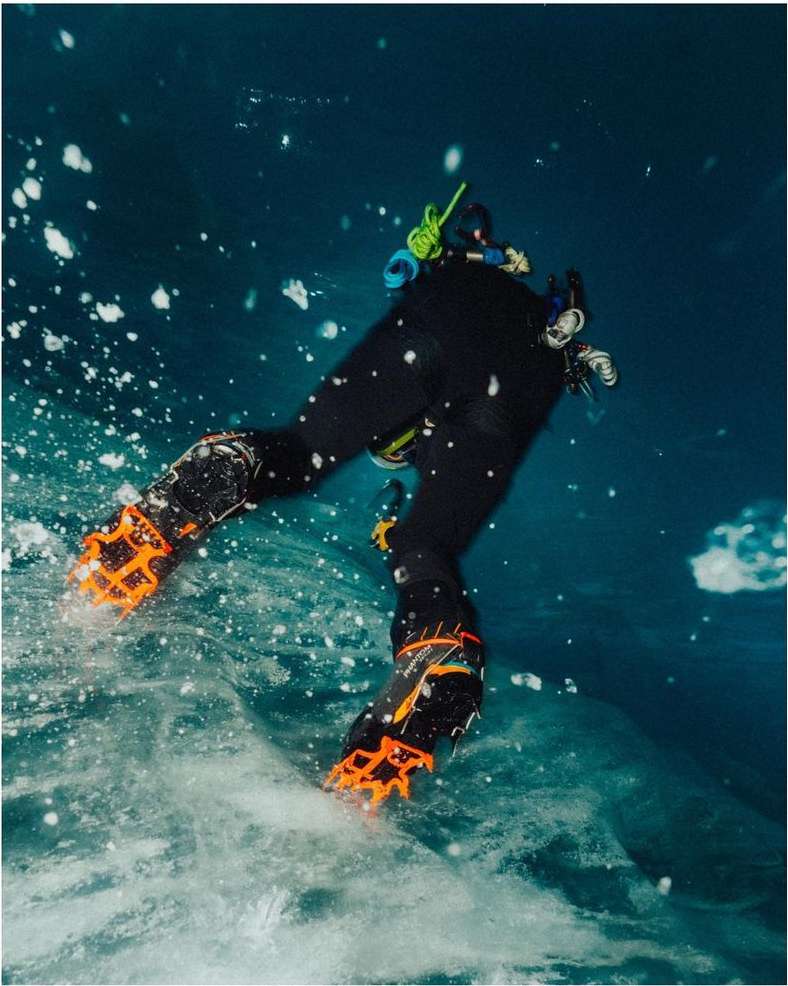 Ice diver in a black suit and orange boots with splashes of water on a blue sea during the day. 
