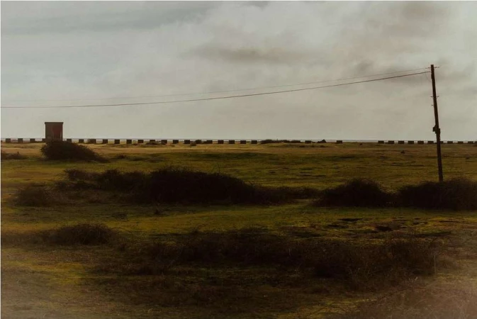 Wide landscape shot of a flat grassy field under an overcast sky with a utility pole and low coastal horizon