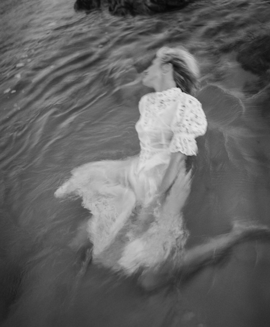 Dreamy monochrome image of a woman in a lace dress immersed in water with long exposure, creating a sense of movement and ethereal beauty.