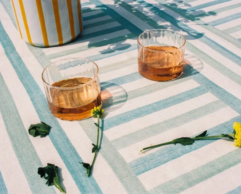 Still life with two glasses of liquid, flowers and a striped container on a blue and white striped surface, creating a summery mood.