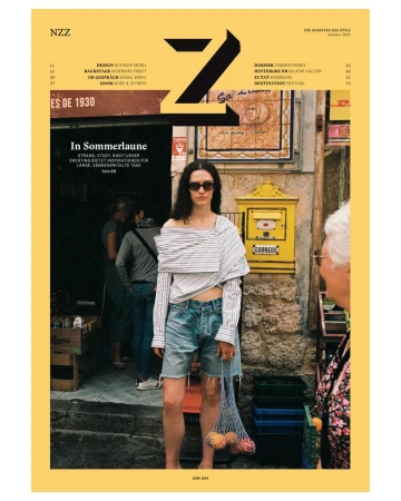 Magazine cover featuring a woman in a striped top and denim shorts, standing in front of a stone building with a yellow mailbox.