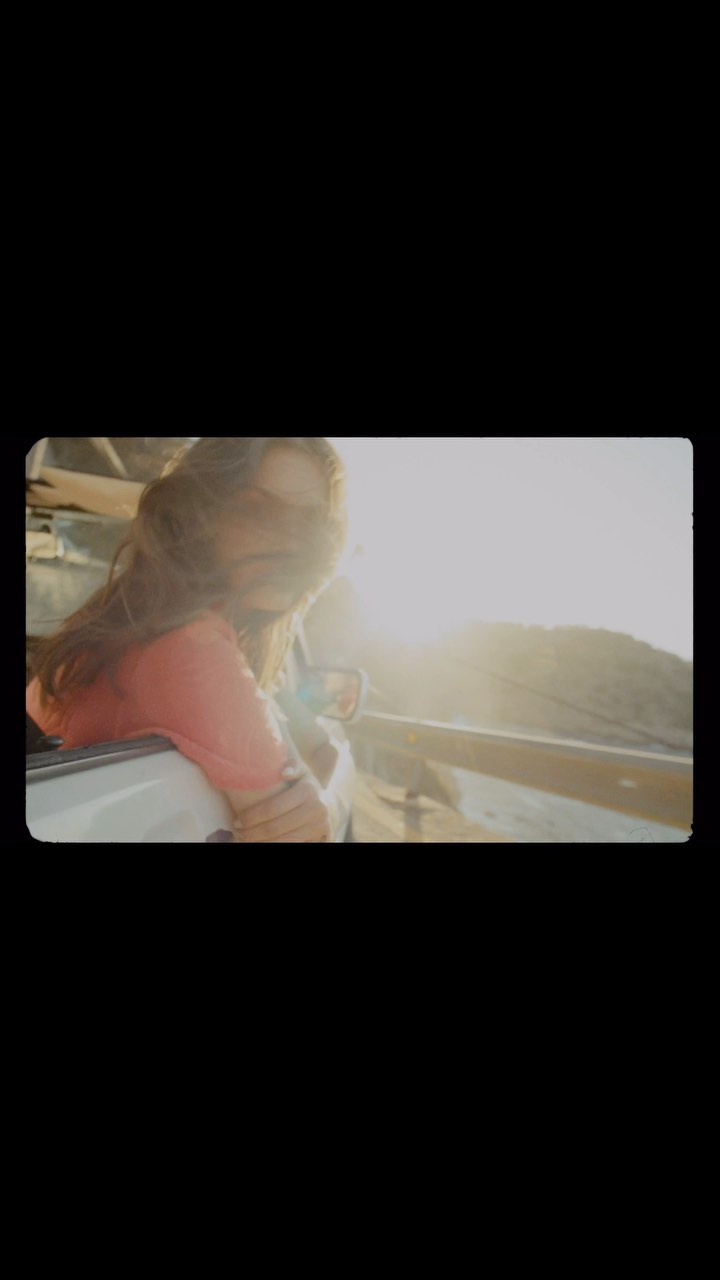 A woman leans out of a car window with hair blowing in the wind, bathed in warm sunlight, capturing a sense of freedom and adventure.