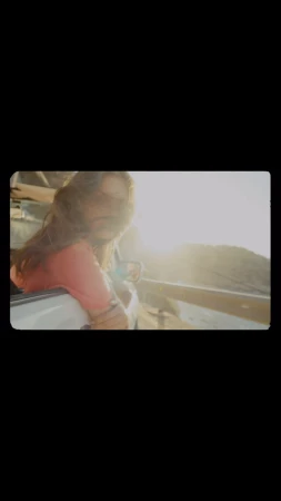 A woman leans out of a car window with hair blowing in the wind, bathed in warm sunlight, capturing a sense of freedom and adventure.