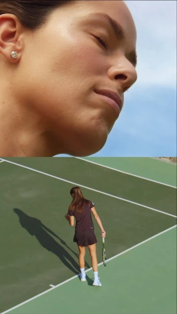 Female tennis player on a green outdoor court with a partial sky view in the background. Tennis player is seen from the back.
