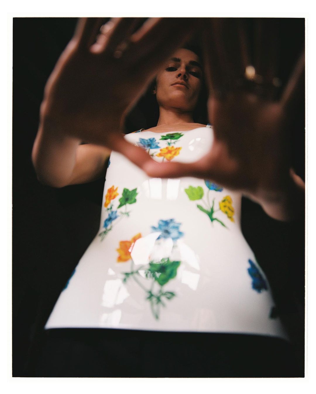 Low angle view of an adult female wearing a floral top, looking down, and framing her face with her hands in a dark environment.
