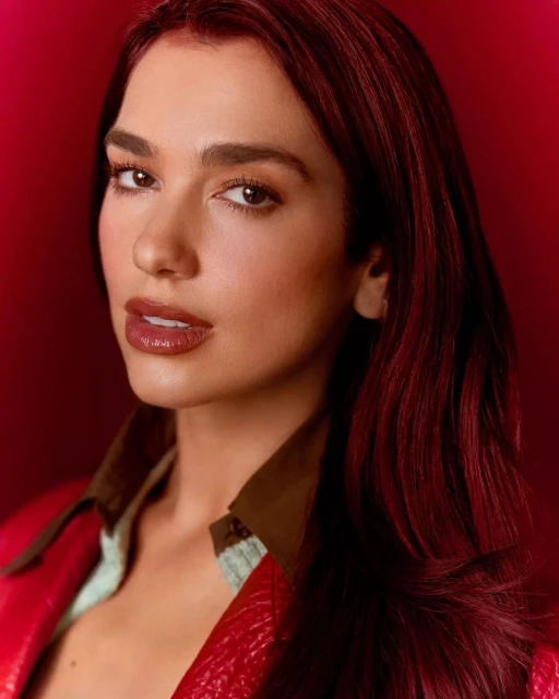 Close-up portrait of a brunette woman with burgundy hair, brown eyes, and glossy lips, wearing a red leather jacket against a red backdrop.