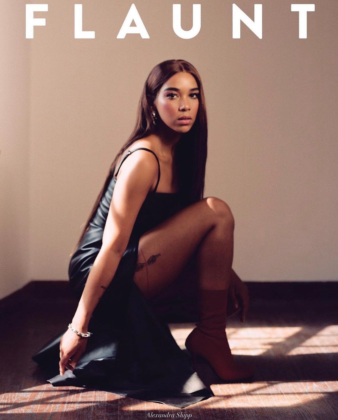 Alexandra Shipp poses in a black dress and brown boots for Flaunt magazine. The portrait is captured indoors with soft, diffused lighting.