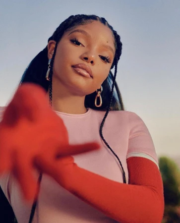 Portrait of young Black woman in pink top and red sleeves wearing braided hair against clear sky