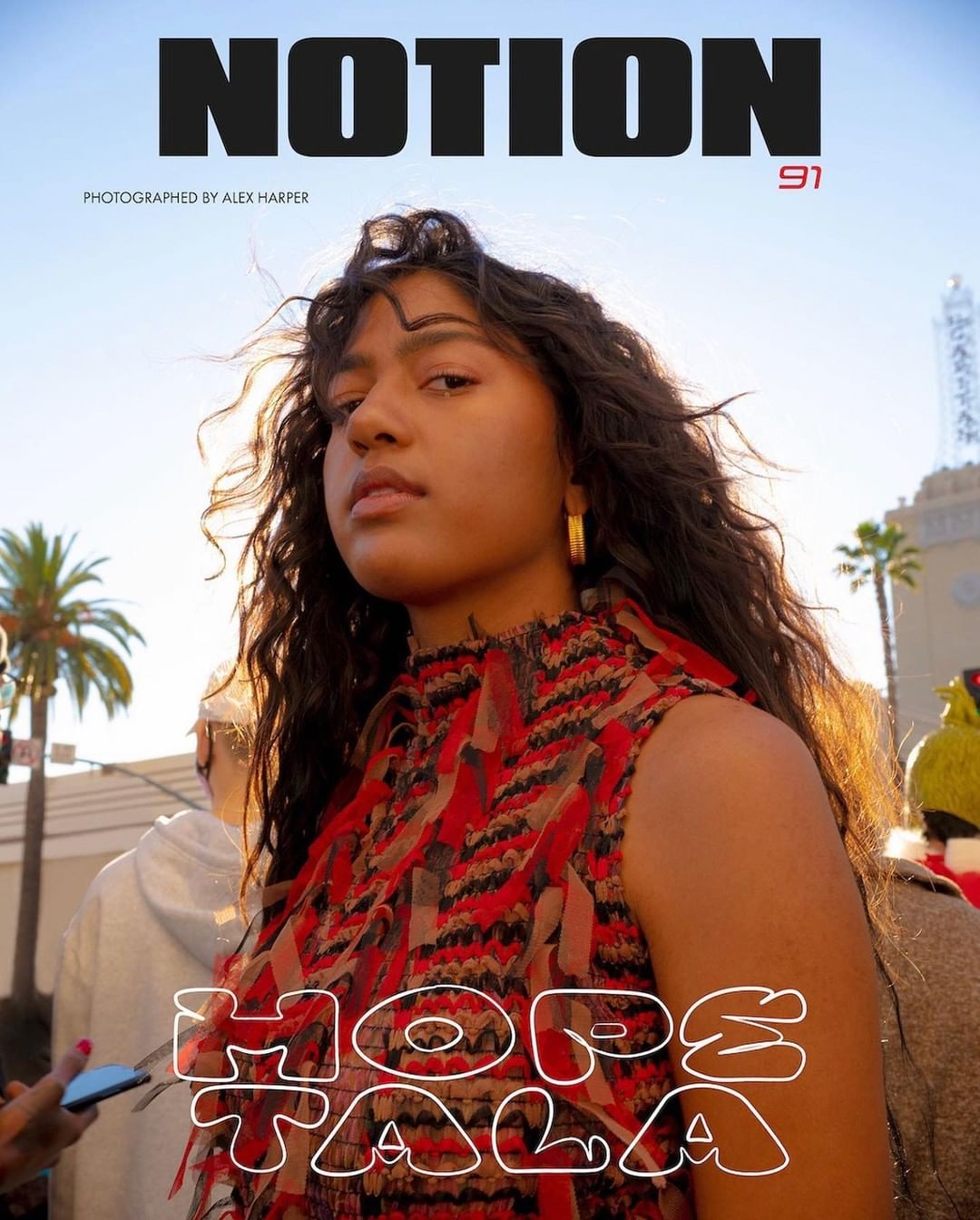 Magazine cover featuring Hope Tala wearing a patterned dress, outdoor setting with palm trees in the background, illuminated by warm, golden light.