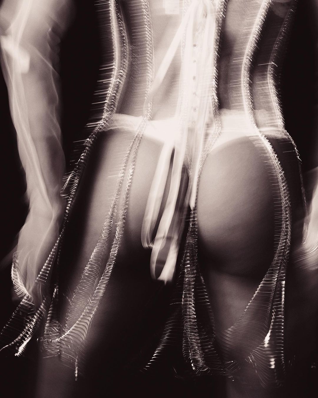 Abstract photograph of a slender female torso and back with lacing details, set against a dark background, using long exposure photography.