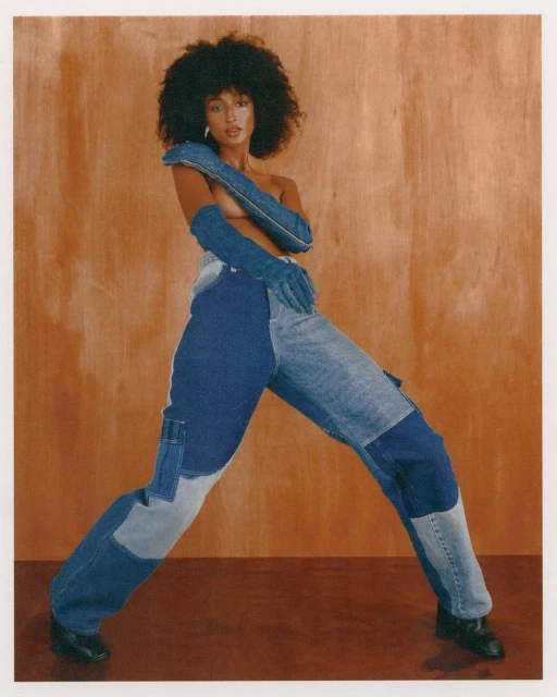 Fashion portrait of an adult woman in a pose wearing denim patchwork jeans and long denim gloves in front of a neutral backdrop.